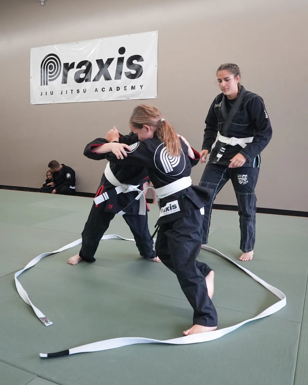 Young students drilling takedowns while a coach supervises at Praxis Jiu Jitsu