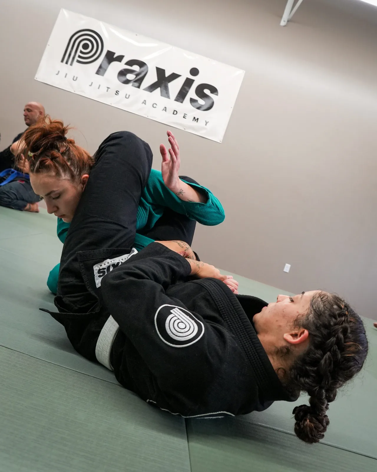Two women training together under the Praxis Jiu Jitsu Academy banner